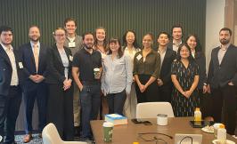 A group of students standing with an alumnus in a conference room.